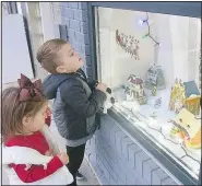  ?? ?? Youngsters enjoy gazing at the structures in the Christmas village in the front windows of the Gravette Public Library on Dec. 4. These two were among the many children lining the sidewalks and passing time while waiting for the parade to start. (NWA Democrat-Gazette/Susan Holland)