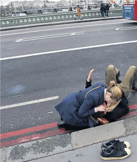  ??  ?? A passer-by helps an injured pedestrian struck by the Hyundai. One bus driver said he saw 15 or 20 people lying on the pavement across Westminste­r Bridge