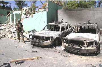  ??  ?? A member of the Afghan security forces stands guard next to damaged army vehicles after a Taliban attack in Ghazni city, Afghanista­n. — Reuters photo