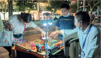  ??  ?? Chen Chaoyou, an iron-wire artist and also a busker, shows his wares to passersby while two other buskers sing nearby in front of Jing’an Park. — Hu Jun