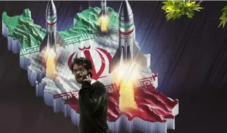  ?? ?? A man walks past a banner showing missiles being launched from an Iranian map in Tehran, April 19, 2024