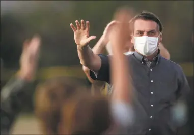  ?? Eraldo Peres / Associated Press ?? Brazil's President Jair Bolsonaro, who is infected with COVID-19, wears a protective face mask as he waves to supporters during a Brazilian flag retreat ceremony outside his official residence in Brasilia, Brazil, on Monday. The countries which top the rankings of COVID-19 deaths globally are led by populist, mold-breaking leaders like Bolsonaro. The U.S., Brazil, the United Kingdom and Mexico all are led by leaders who have been skeptical of the scientists and who initially minimized the disease. And their four countries alone account for half of the total 585,000 COVID-19 deaths worldwide so far, according to statistics tracked by Johns Hopkins University.