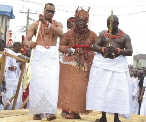  ??  ?? BENIN CITY: Newly crowned 40th Oba, or king, of the Benin kingdom, Oba Ewuare II (C), walks on a wooden bridge assisted by palace aides to perform the rite during his coronation. — AFP