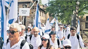  ?? ?? Participan­ts hold Israeli flags as they walk under the famous camp gate with the motto Arbeit Macht Frei (Work brings freedom)