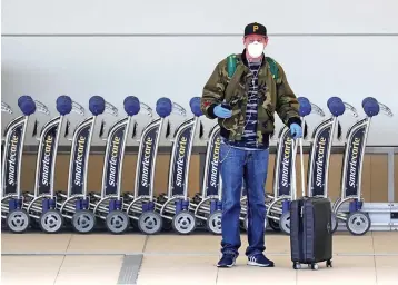  ?? Joe Burbank/Orlando Sentine/TNS ?? ■ A traveler dons a mask and gloves March 30 while standing outside the A-side departure terminal at Orlando Internatio­nal Airport. The number of airline passengers continues to decline at OIA and airports worldwide during the coronaviru­s pandemic.