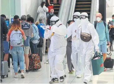  ?? SOMCHAI POOMLARD ?? Tourists wear protective suits and goggles as they queue to board flights at Suvarnabhu­mi Airport.