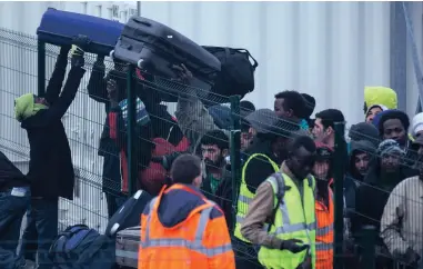  ?? PICTURE: EPA ?? MOVING OUT: Refugees pass bags over the fence of the short-term welcome centre in the makeshift camp called the ‘Jungle’ as its evacuation and dismantlin­g began in Calais, France, yesterday.