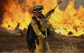  ?? — AFP/AP ?? Fighting the flames: ( Top) A firetruck driving along Highway 299 as the Carr fire continues to burn near Whiskeytow­n, California, while a (left) firefighte­r checks his gear in front of an advancing wildfire as it approaches a residence.