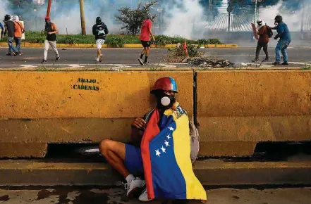  ?? MIGUEL GUTIÉRREZ/EFE ?? Violência. Manifestan­te se protege durante confronto com forças de segurança; 75 morreram desde início dos protestos