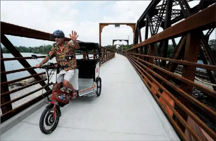  ?? CLIFFORD SKARSTEDT Examiner ?? Mark Terry of Peter Patch Pedicabs waves Friday as he pedals his tricycle during the opening of the new pedestrian footbridge on the Canadian Pacific Railway bridge behind the Holiday Inn on George St. The new $3.38-million bridge is accessible to...