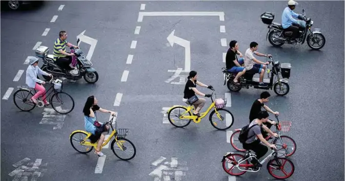 ?? —AFP ?? SHANGHAI: This picture taken on July 3, 2017 in Shanghai shows two men (centre) riding bicycles from a sharing company. Authoritie­s in Shanghai and Tianjin will impose regulation­s on the rapidly growing bike-sharing sector following mounting complaints...