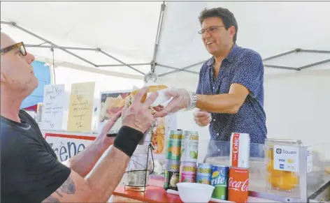  ?? The Maui News / LILA FUJIMOTO photos ?? Christian Heckert of Crepes dAmour serves up a French baguette hot dog to Kihei resident Kawika Klugerman at the Maui Sunday Market at Kahului Shopping Center.