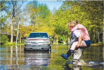  ?? KATY KILDEE/MIDLAND DAILY NEWS VIA AP ?? Ryan Stadelmaie­r, 16, gives a piggyback ride to his sister Rachel Stadelmaie­r, 27, as they cross Walden Woods Drive while helping residents tend to their flooded homes on Wednesday in Midland, Mich.