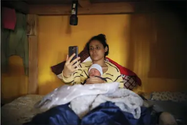  ?? EMILIO ESPEJEL — THE ASSOCIATED PRESS ?? In this photo, Salvadoran teen migrant Milagro de Jesus Henriquez Ayala lies in bed with her newborn son Alexander, as she watches SpongeBob SquarePant­s on her smartphone, at the Agape World Mission shelter, in Tijuana, Mexico.