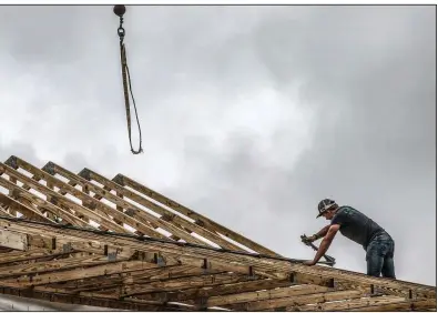  ??  ?? Jaden Chanley with J.R.J. Constructi­on secures a roof truss Tuesday atop a house going up near Ensor, Ky. The Commerce Department says new home constructi­on starts nose-dived in April.