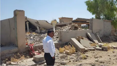  ?? (Stephen Kalin/Reuters) ?? KURDISH SHOP owner Abu Suhail stands in front of a destroyed home inside Zumar village, Iraq, last year.