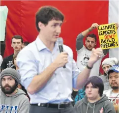  ?? JONATHAN HAYWARD / THE CANADIAN PRESS ?? Protesters hold up signs Friday as Prime Minister Justin Trudeau speaks at a public town hall in Nanaimo, B.C.