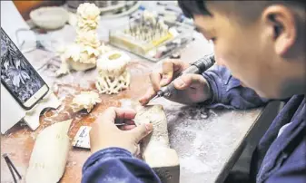  ??  ?? Guo Chen carves a piece of ivory at his desk at the Beijing Ivory Carving Factory.