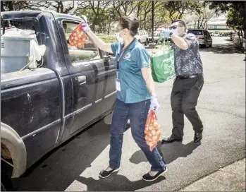  ?? The Maui News / TERRIE ELIKER photo ?? Shirley Blackburn from Maui County Mayor Michael Victorino’s budget office and Tyson Miyake, Victorino’s chief of staff, hand out bags of produce at the Upcountry Pool parking lot in Pukalani on March 30. Hundreds of cars snaked up and down Old Haleakala Highway and across Makawao Avenue as part of a giveaway to “people in need” organized by Pukalani Superette with partners Sysco Hawaii and the County of Maui. Federal CARES Act funds were used on food giveaways in partnershi­p with local businesses and farmers.