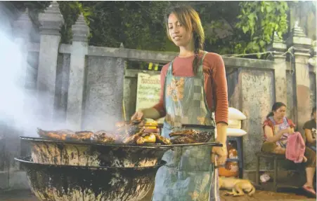  ?? PHOTOS: ANDREW MARSHALL ?? A Thai woman grills chicken at a roadside stall in Bangkok's Banglamphu district.