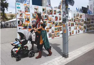  ?? (Carlos Garcia Rawlins/Reuters) ?? A FAMILY in costume walks past placards with pictures of hostages kidnapped in the October 7 attack, in Tel Aviv yesterday.