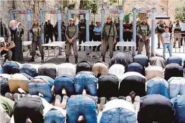  ??  ?? WARGA Palestin bersolat di luar pagar keselamata­n Israel sambil dikawal tentera Zionis.