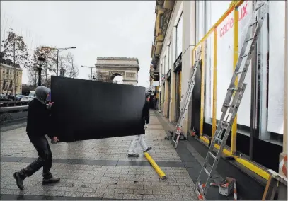  ?? Francois Mori The Associated Press ?? Workers carry a wooden piece to protect shop windows Friday on the Champs-elysees in Paris. The Arc de Triomphe is seen in the background. Heavy security will put central Paris in a virtual lockdown Saturday.