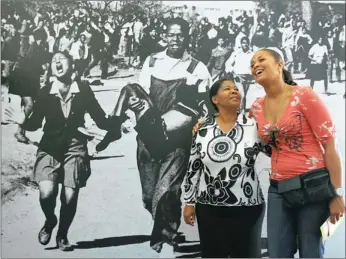  ?? PICTURE: CHRIS COLLINGRID­GE ?? Antoinette Sithole, sister of the late Hector Pieterson, stands with Laila Ali in front of the dramatic photo in the Hector Pieterson Museum of the dying boy being carried from the 1976 Soweto riots by Mbuyisa Makhubu.