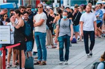  ?? JONATHAN NACKSTRAND/GETTY ?? A man wearing a mask walks past people not wearing masks in Stockholm, Sweden, where COVID-19 restrictio­ns have been more lax than in the United States.