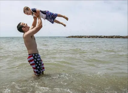  ?? Steph Chambers/Post-Gazette photos ?? Jesse Vance, of Vandergrif­t, lifts his son Eli, 4, out of the water at Presque Isle State Park in Erie.