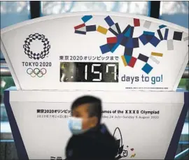  ?? Jae C. Hong Associated Press ?? THE CORONAVIRU­S has some health officials questionin­g the wisdom of mass gatherings. A man in Tokyo passes by an Olympics countdown clock last month.