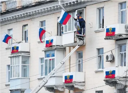  ?? Photo / AP ?? Workers hang Russian flags at an apartment building in Luhansk after referendum­s were held in the region last week.