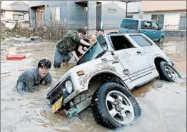  ?? JIJI PRESS/GETTY-AFP ?? Residents try to right a vehicle stuck in a flooded area Monday in Okayama prefecture. Authoritie­s in Japan worked to reach people feared trapped by flooding.