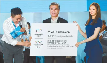  ?? Korea Times photo by Koh Young-kwon ?? President Moon Jae-in holds an oversized name card showing he has been named honorary ambassador for the PyeongChan­g Olympic and Paralympic Winter Games, after receiving it from former national figure skating star Kim Yuna, right, during an event to...