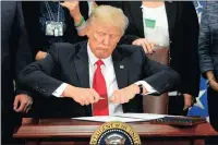  ??  ?? President Donald Trump takes the cap off a pen before signing an executive order to build a wall on the Mexican border.