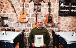  ??  ?? Andreas Duskos holds a catalogue bearing a picture of Cohen and a poem he wrote dedicated to the tavern at a tavern Cohen used to go on Hydra. — AFP photos