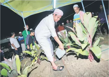  ??  ?? Md Sukri Yassin pours water on his son’s grave at the Tanah Perkuburan Taman Ibukota, Setapak. — Bernama photo