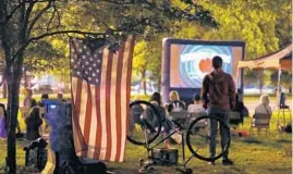  ?? CHRIS SWEDA/CHICAGO TRIBUNE ?? A U.S. flag hangs from a tree branch as people watch a Looney Tunes animated short outside the Comfort Station.