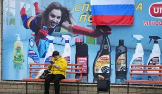  ?? ?? A woman waits at a bus stop with an advertisin­g poster, a day after voting in four Moscow-held regions of Ukraine on referendum­s to become part of Russia.