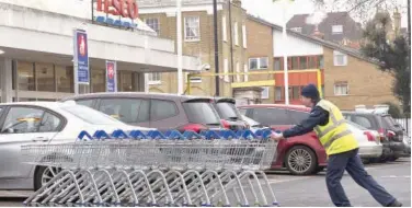  ?? Agence France-presse ?? ↑ A worker pushes trolleys in the car parking lot at a branch of Tesco in south London.