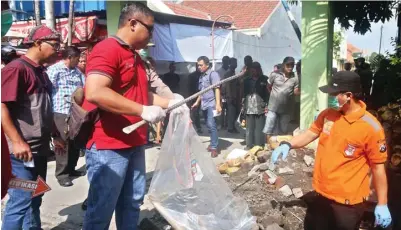  ?? BOY SLAMET/JAWA POS ?? AMANKAN BUKTI: Petugas polresta memasukkan cangkul dan linggis ke plastik serta mengevakua­si jenazah Mamuk dari tempat kejadian perkara kemarin.