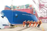  ?? — Reuters ?? Workers wearing face masks helping a container ship to its berth at Qingdao port in Shandong province.