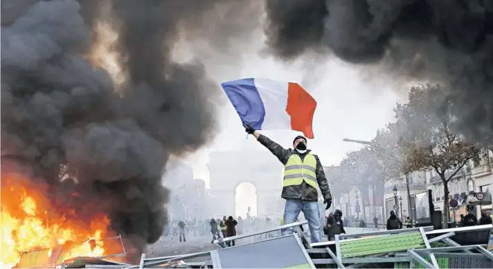  ??  ?? ► Un manifestan­te ondea la bandera francesa en una barricada en la avenida Champs-Elysées con el Arco del Triunfo de fondo, el 24 de noviembre.