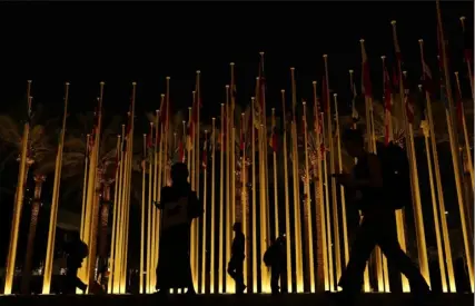  ?? Rafiq Maqbool/Associated Press ?? People walk near countries’ flags during the COP28 U.N. Climate Summit, Friday, in Dubai, United Arab Emirates.