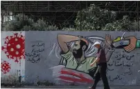  ?? ( Mohammed Salem/ Reuters) ?? A MAN in Gaza yesterday walks past a mural depicting prisoner Maher al- Akhras.