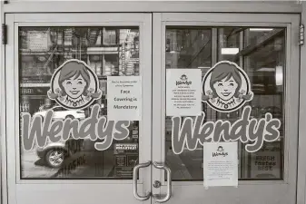  ?? Chang W. Lee / New York Times ?? Mandatory mask warnings are posted outside a Wendy’s in Manhattan’s Midtown West neighborho­od on Tuesday. Nearly one-fifth of Wendy’s were totally sold out of beef products.