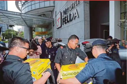  ?? PIC BY ASYRAF HAMZAH ?? Malaysian Anti-Corruption Commission officers, escorted by auxiliary police officers, loading boxes of seized documents into a car following a raid at Menara Felda in Kuala Lumpur yesterday.