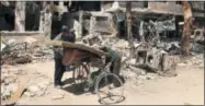  ?? THE ASSOCIATED PRESS ?? Men load a carpet and mattress onto a bicycle Monday in front of damaged buildings in the town of Douma, the site of a suspected chemical weapons attack near Damascus, Syria.