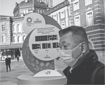  ?? BEHROUZ MEHRI/AFP VIA GETTY IMAGES ?? A man wearing a face mask amid concerns over the spread of the COVID-19 coronaviru­s walks past the Olympic Games countdown clock outside Tokyo station on Tuesday.