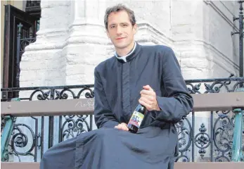  ?? FOTO: DPA ?? Pfarrer Jérémie Schaub präsentier­t eine Flasche „Ste Kat“Craft-Bier auf einer Bank vor seiner Kirche.